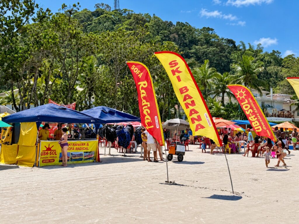 Barracas de praia com bandeiras coloridas de Sofá Radical e Ski Banana na areia de Ubatuba