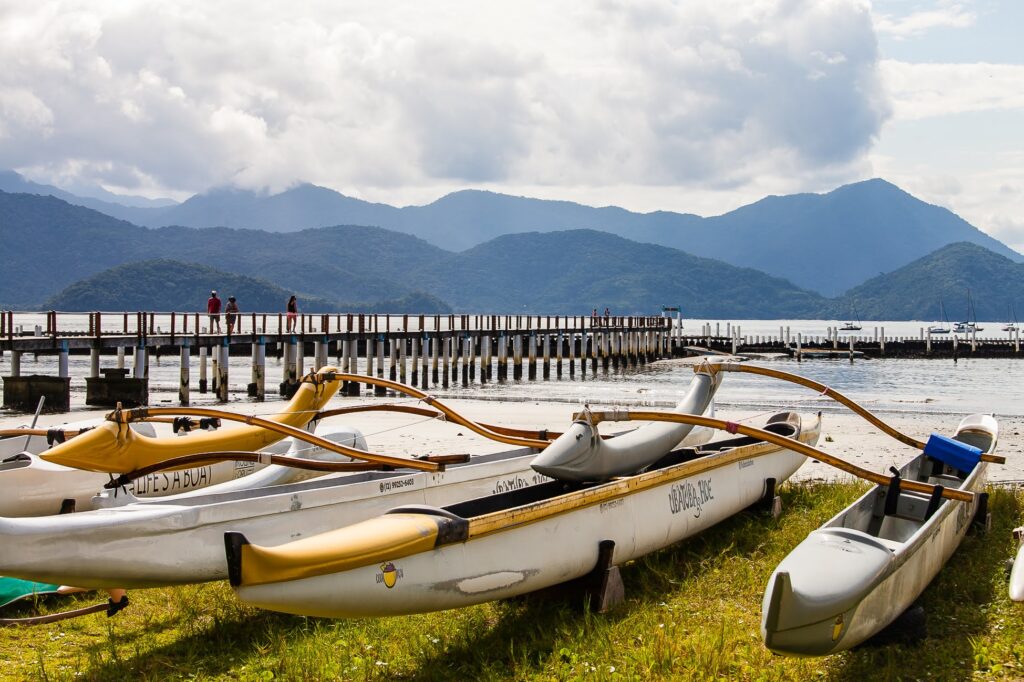 Canoas havaianas estacionadas na areia com deck e serra ao fundo em Ubatuba