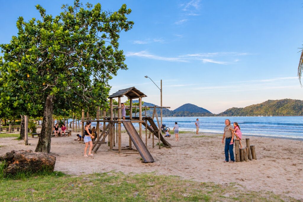 Parque infantil de madeira na areia com pessoas e o mar ao fundo