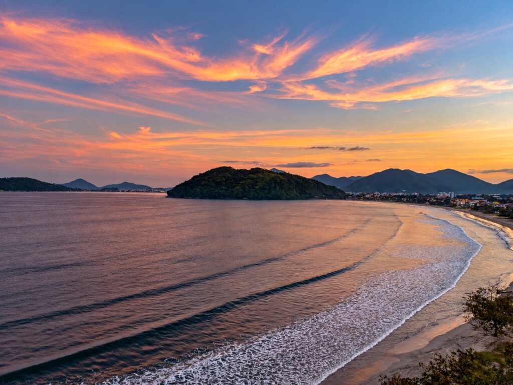 Vista da faixa de areia e do mar ao entardecer sob céu alaranjado e rosado