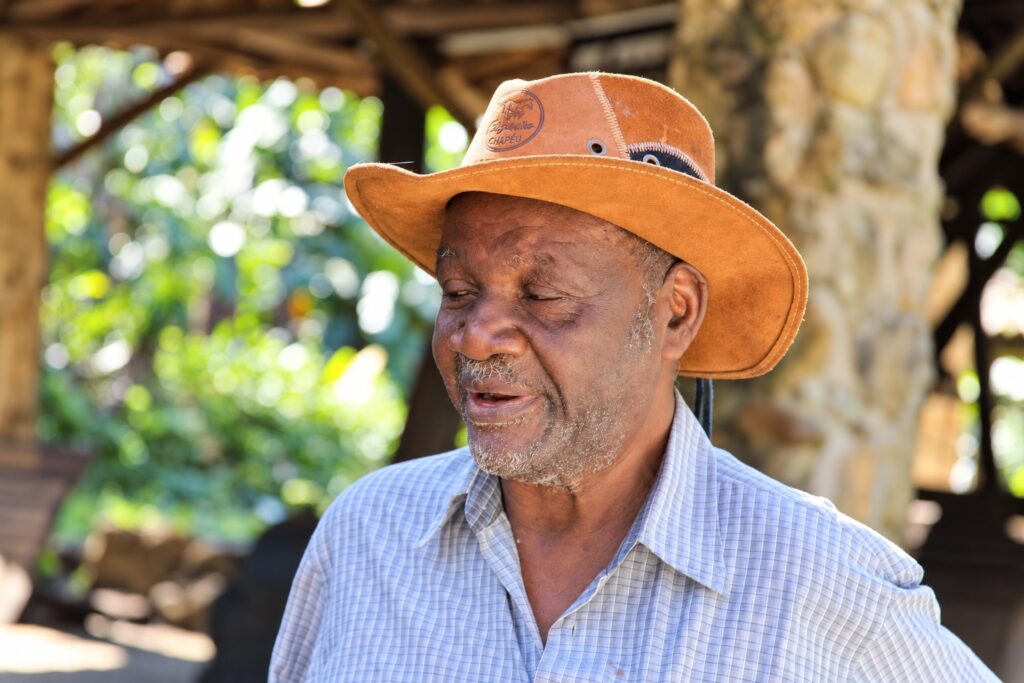 Senhor idoso usando chapéu de couro, contando histórias em ambiente rústico de madeira e pedra