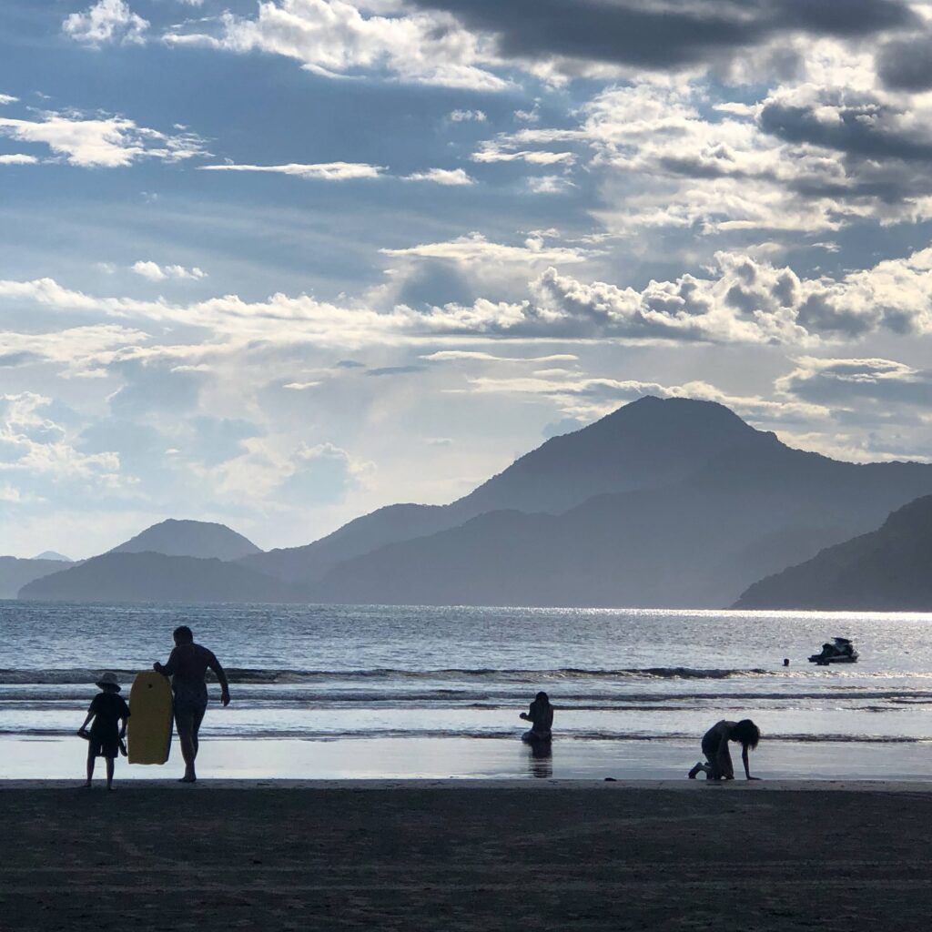 Pôr do sol em Ubatumirim com pessoas na beira da água e serra no horizonte