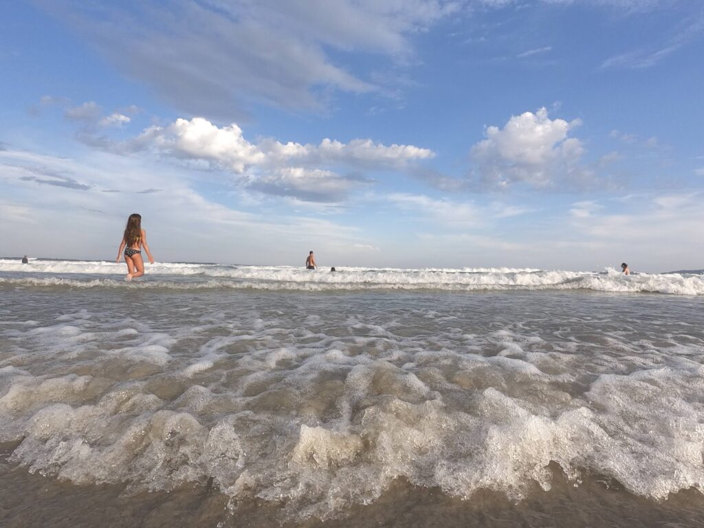 Banhistas entrando no mar com ondas baixas na Praia Grande em Ubatuba, em dia de sol