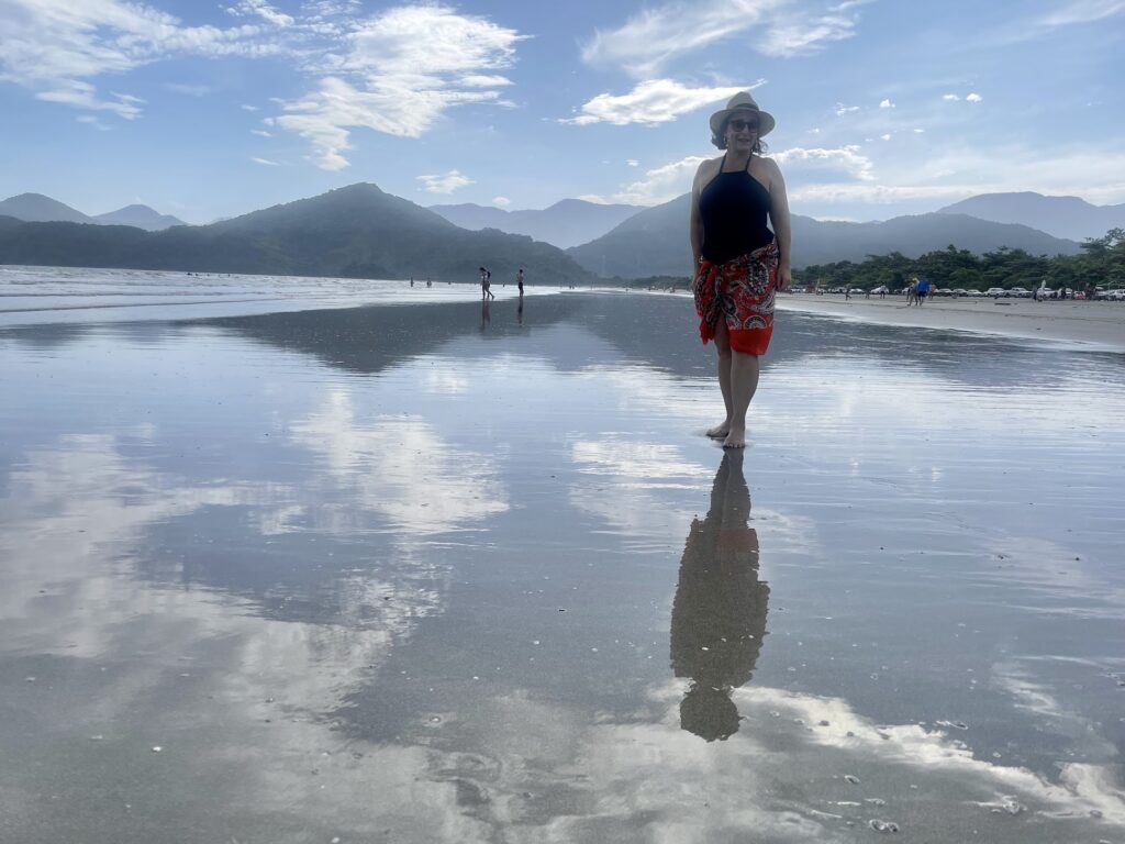 Pessoa caminhando na areia molhada de Ubatumirim com reflexo no espelho d’água