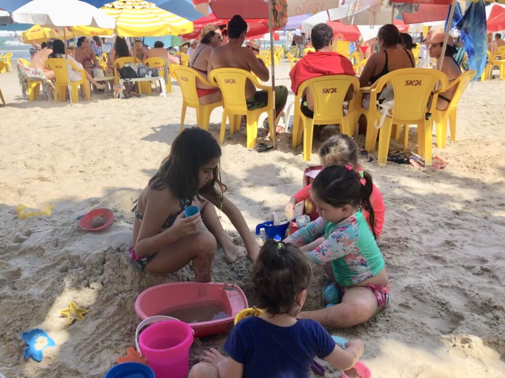 Famílias e crianças brincando na areia com cadeiras de praia e guarda-sóis na Praia Grande em Ubatuba