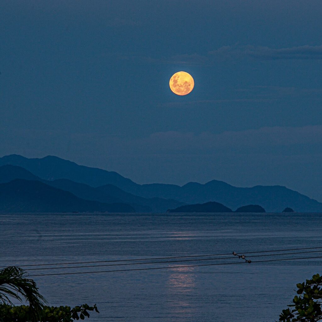 Lua cheia sobre o mar na orla de Ubatuba, com morros ao fundo